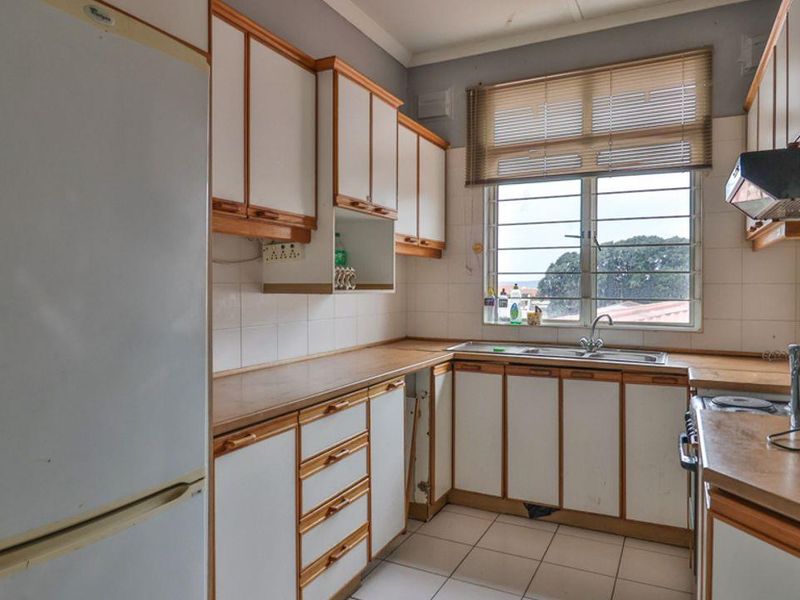 A functional kitchen featuring laminate countertops, built-in cabinetry, and a stainless steel sink, with some visible wear to the cabinetry and base panels.