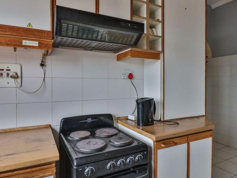 A dated kitchen featuring built-in cabinetry, a tiled backsplash, and an electric stove with an overhead extractor fan.