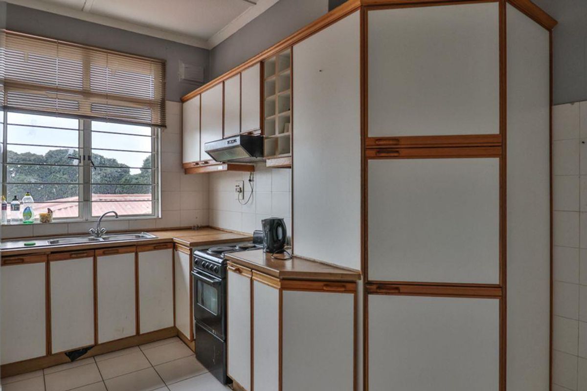 A functional kitchen featuring white cabinetry with timber trim, tiled backsplash, stainless steel sink, and a freestanding stove.