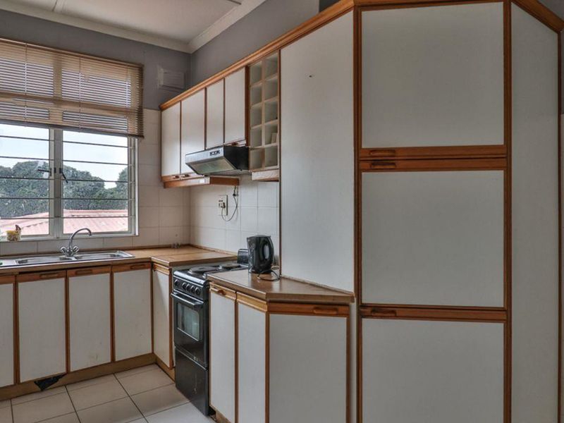 A functional kitchen featuring white cabinetry with timber trim, tiled backsplash, stainless steel sink, and a freestanding stove.
