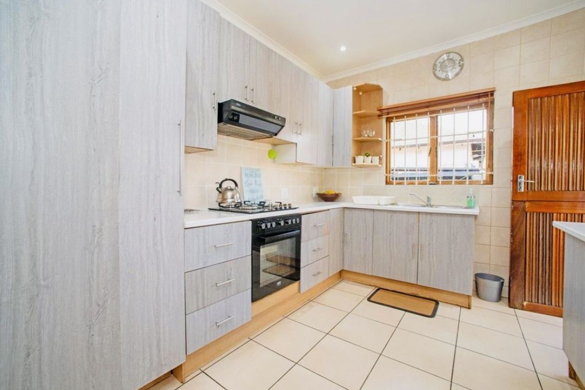 A functional kitchen featuring light wood-grain cabinetry, a gas hob with extractor, built-in oven, double sink, and tiled finishes throughout.