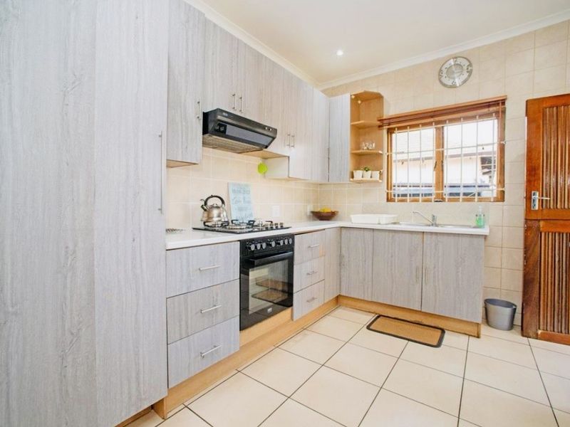 A functional kitchen featuring light wood-grain cabinetry, a gas hob with extractor, built-in oven, double sink, and tiled finishes throughout.