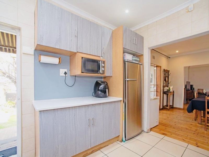 A functional kitchen area featuring built-in cabinetry, tiled splashbacks, and tiled flooring, with direct access to an outdoor patio area.