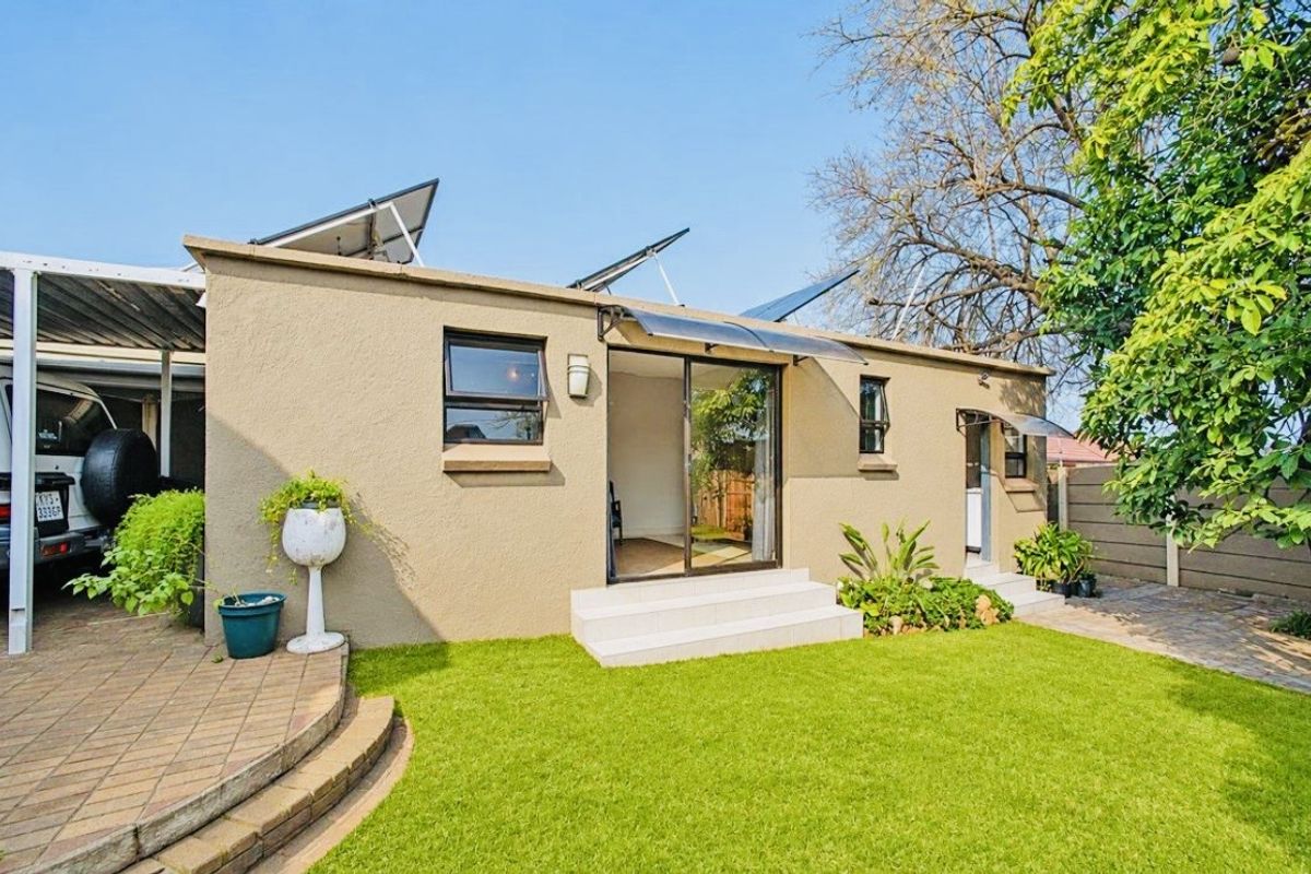 Rear exterior view featuring a paved patio, lawn, sliding glass door access, and roof-mounted solar panels.