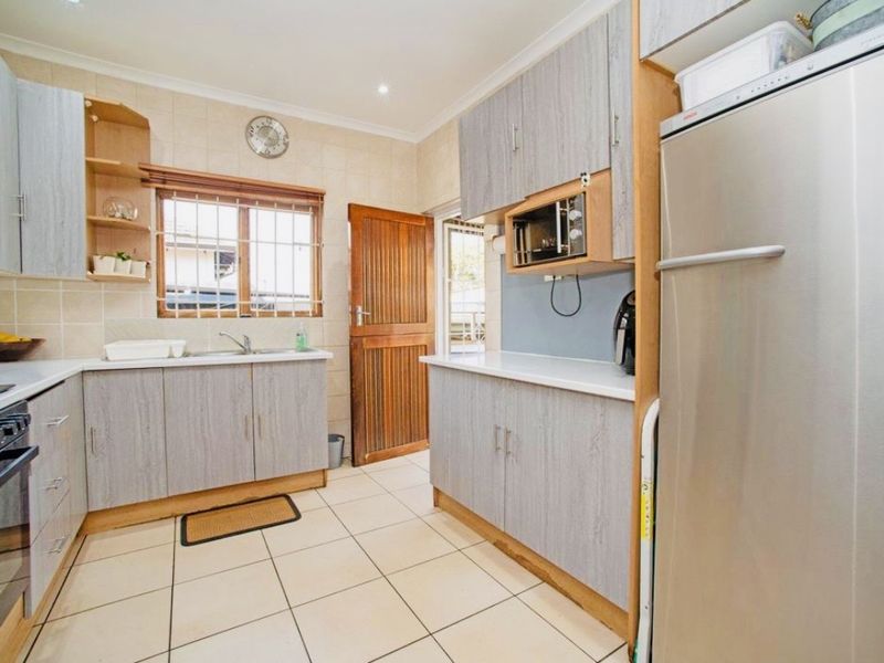 Functional kitchen featuring light wood-grain cabinetry, tiled flooring, built-in oven and hob, and ample counter space with a window for natural light.