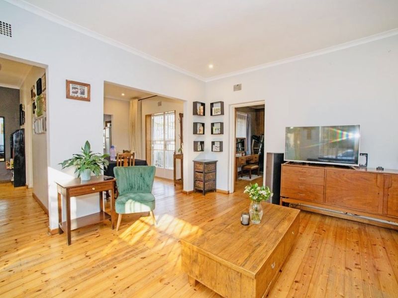 A bright living room featuring polished timber flooring, cove cornicing, and recessed lighting, with an open-plan flow leading to adjacent rooms.