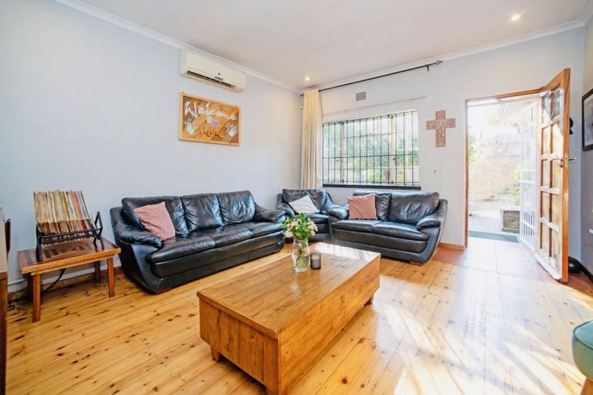 A living room featuring polished timber flooring, an air conditioning unit, and direct access to an outdoor area through a timber door.