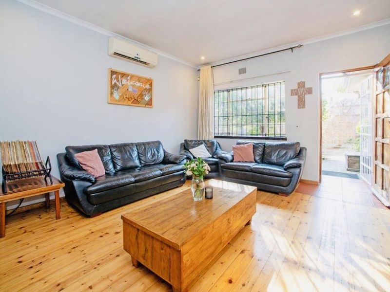 A living room featuring polished timber flooring, an air conditioning unit, and direct access to an outdoor area through a timber door.