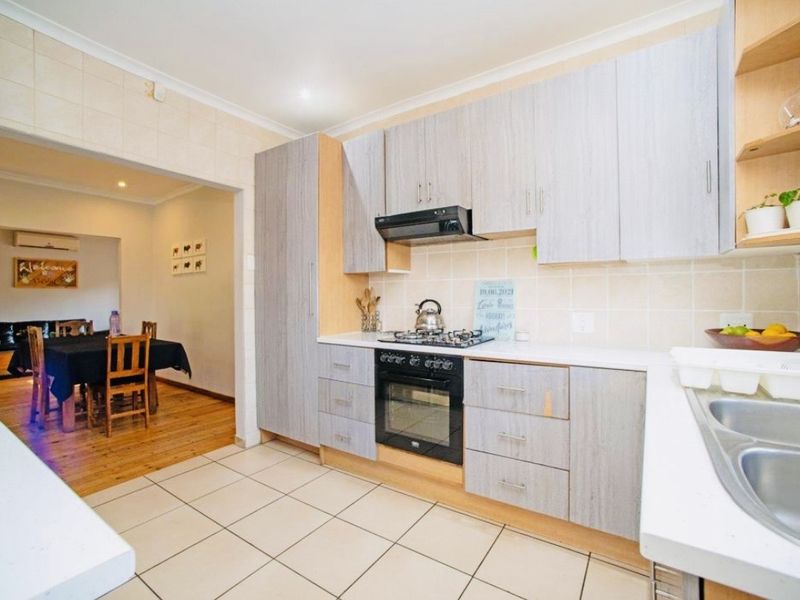 A functional kitchen featuring light wood-grain cabinetry, a gas hob, built-in oven, and tiled splashback, with an adjacent dining area.
