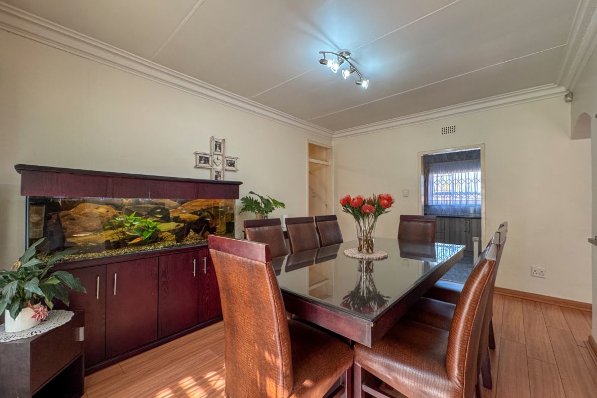 A well-maintained dining room featuring laminate flooring, coved ceilings, and modern track lighting, with a clear view into the adjacent kitchen area.