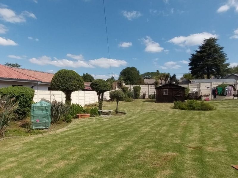 A spacious rear garden featuring a well-maintained lawn, perimeter precast concrete walling with electric fencing, and a tiled roof house elevation.
