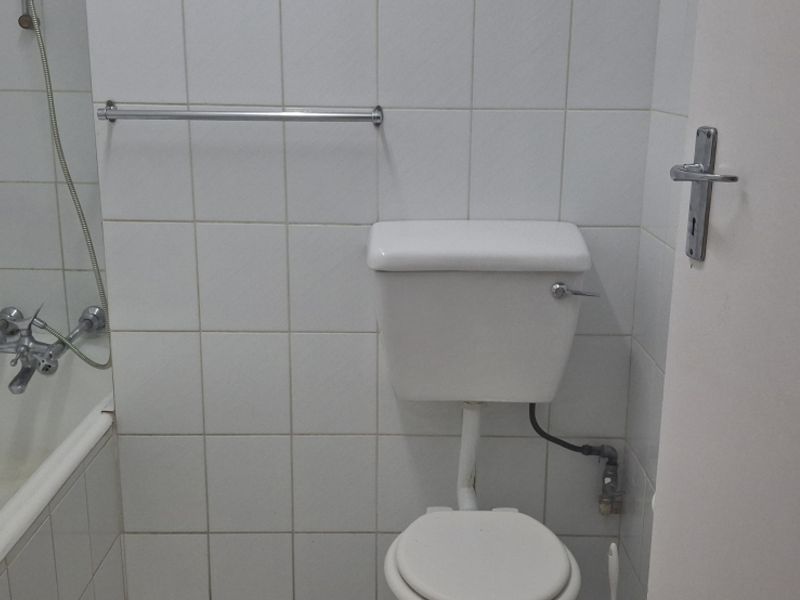 A compact bathroom featuring a standard bathtub, toilet, and white wall tiling. The space is functional but would benefit from modern updates.