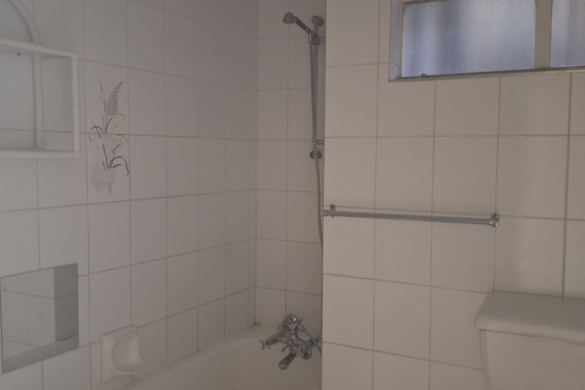 A functional bathroom featuring a bathtub with shower mixer, toilet, and tiled walls, presenting an opportunity for modern renovation and aesthetic updates.