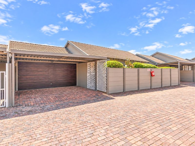 Front exterior view of the townhouse featuring a brick paved driveway, covered carport, and secure wooden garage door with perimeter walling.