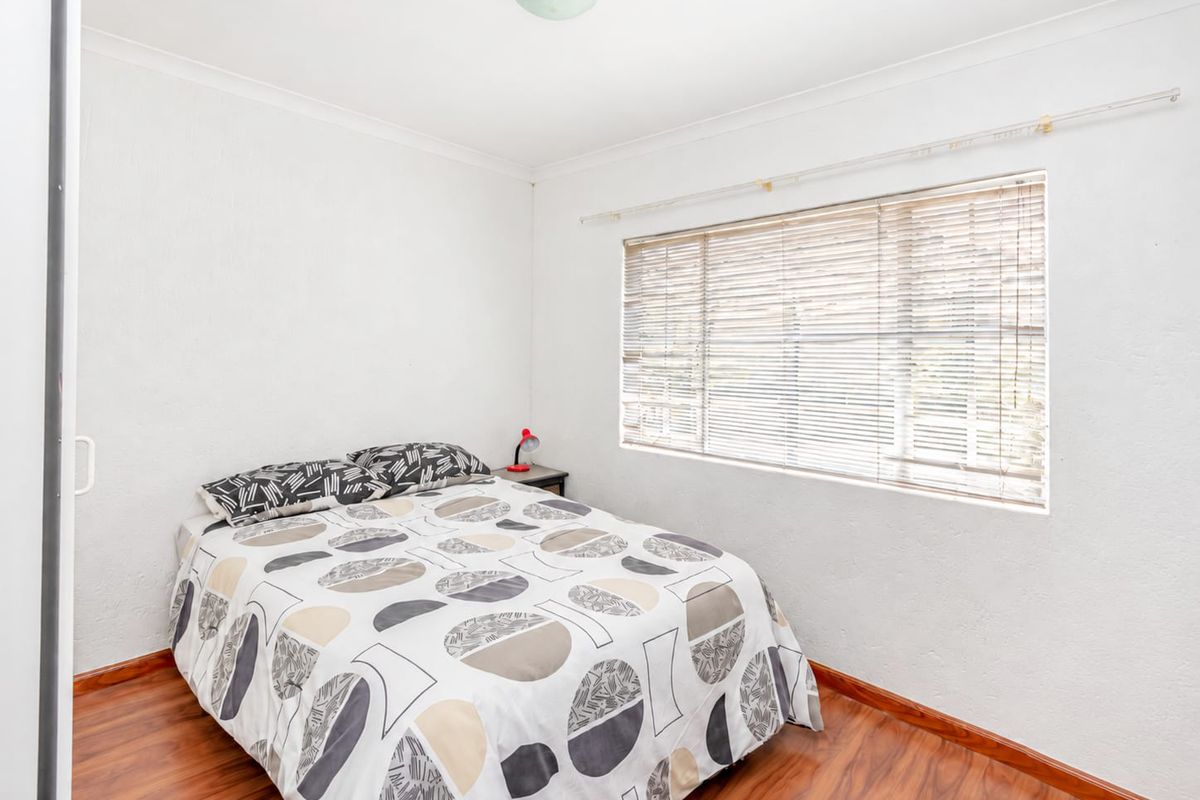 A well-lit bedroom featuring laminate flooring, neutral walls, and venetian blinds, offering a clean and functional living space.