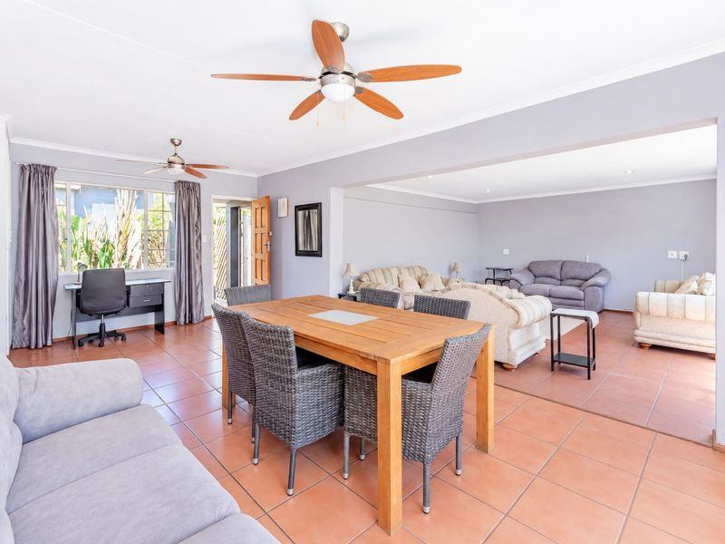 Spacious open-plan living and dining area featuring tiled flooring, dual ceiling fans, and direct access to the exterior through a sliding door.