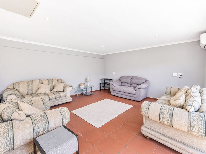 A spacious living room featuring neutral wall tones, tiled flooring, and a wall-mounted air conditioning unit, providing a comfortable and functional living space.