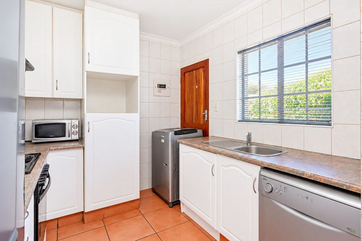 Functional kitchen featuring white cabinetry, laminate countertops, tiled splashbacks, and ceramic floor tiles, with direct access to an exterior door.