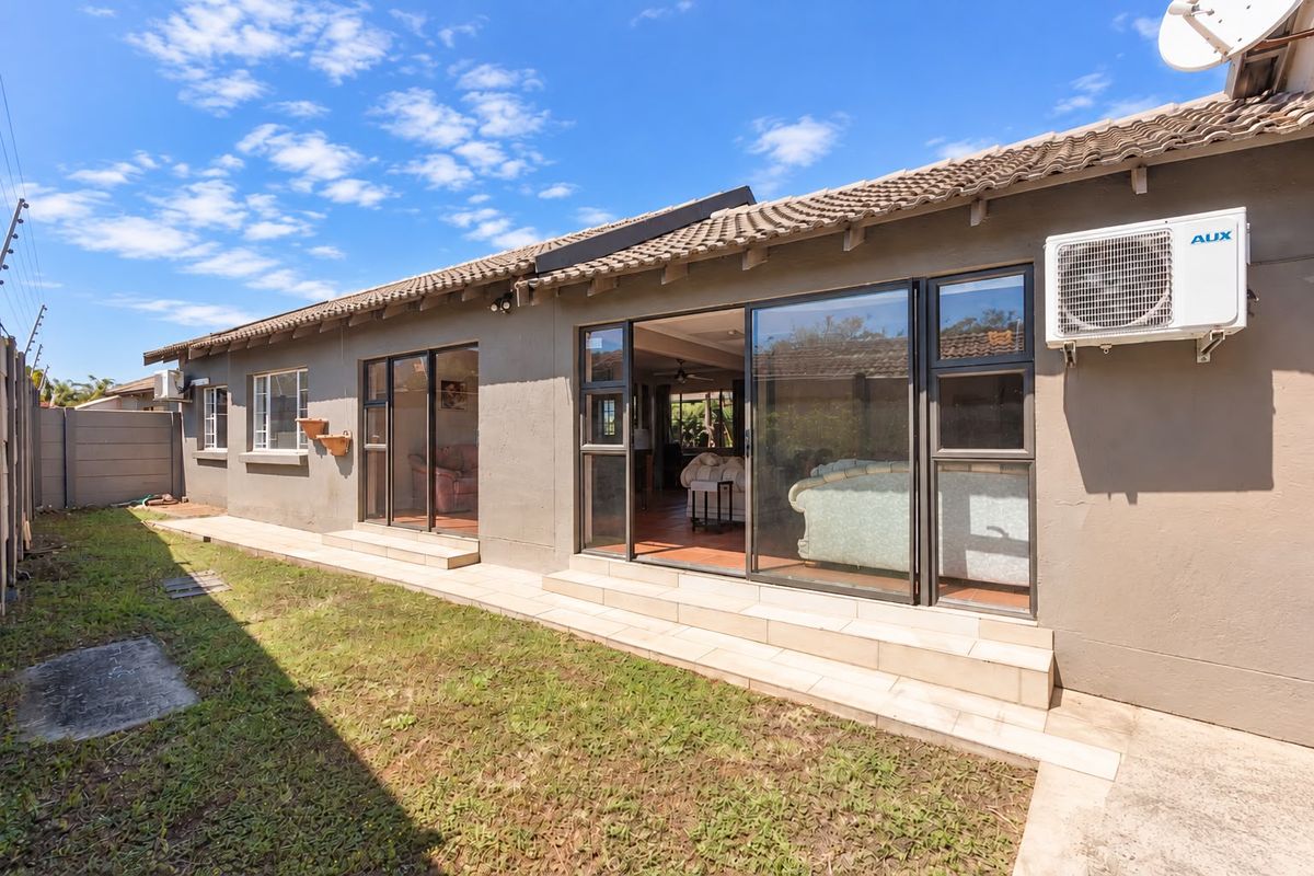 Rear view of the townhouse featuring a tiled roof, sliding glass doors leading to the interior, and a private garden area with boundary wall.
