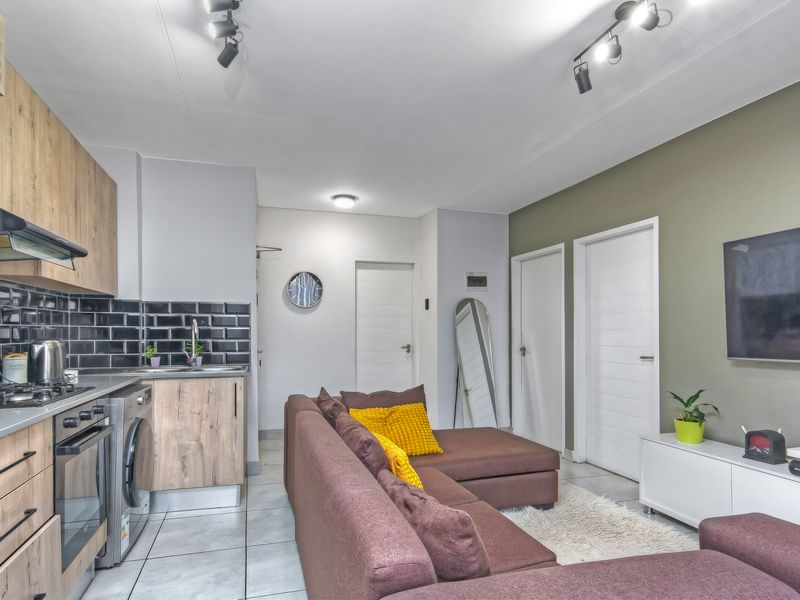 Modern open-plan living area featuring a compact kitchen with wood-finish cabinetry, subway tile backsplash, integrated appliances, and tiled flooring throughout.