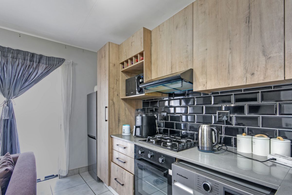 Modern kitchen featuring wood-look cabinetry, black subway tile backsplash, stone countertops, and integrated gas hob with extractor fan.