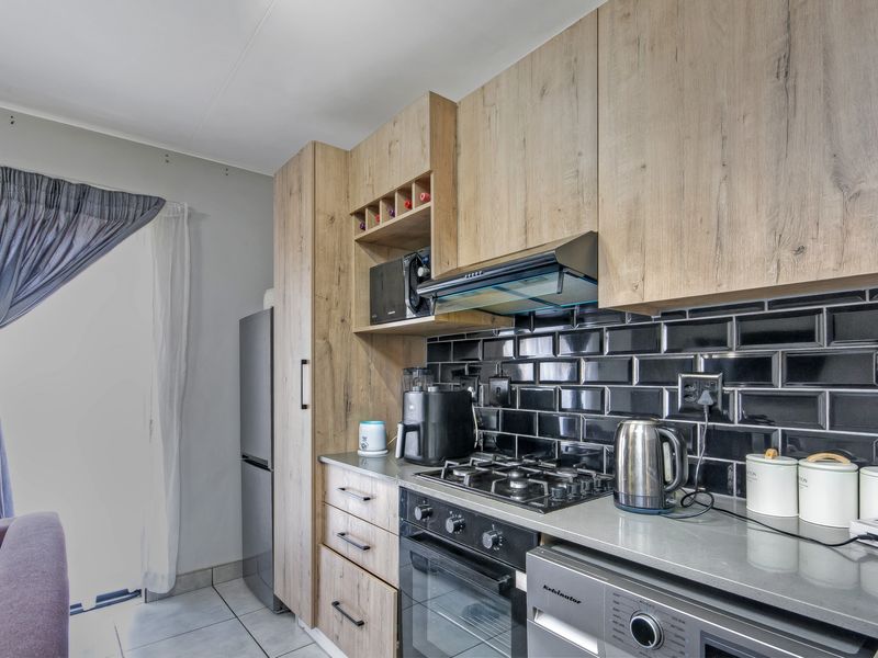 Modern kitchen featuring wood-look cabinetry, black subway tile backsplash, stone countertops, and integrated gas hob with extractor fan.