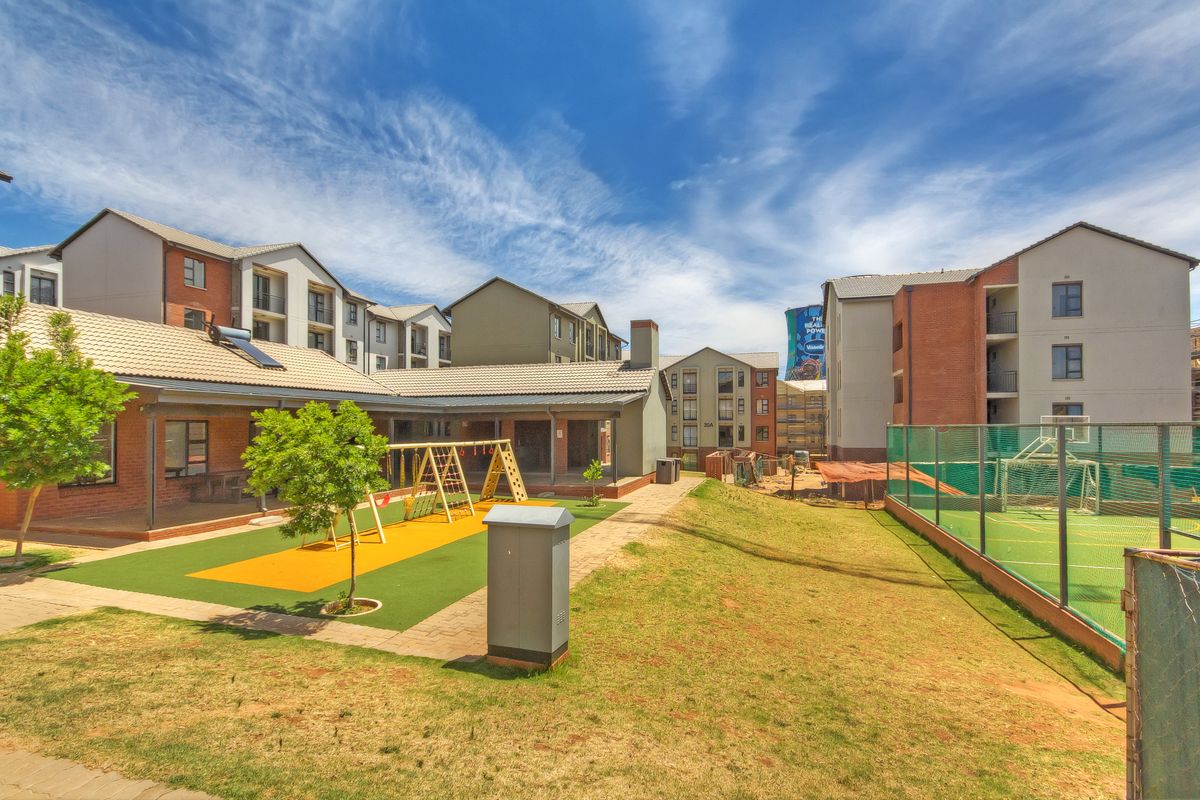 A communal outdoor area featuring a covered patio, a fenced sports court, and a playground set within a well-maintained apartment complex.