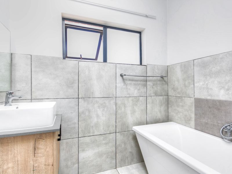 Modern bathroom featuring a vessel sink on a wood-finish vanity, a freestanding bathtub with a handheld shower mixer, and contemporary grey wall tiling.