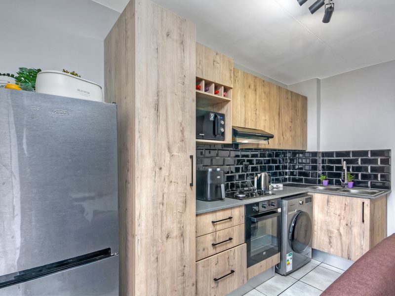 Modern kitchen featuring wood-look cabinetry, black subway tile backsplash, built-in oven, gas hob, and integrated laundry plumbing.