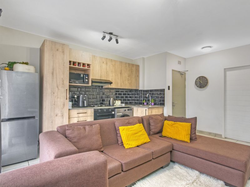 A modern open-plan living area featuring a compact kitchen with wood-finish cabinetry, subway tile backsplash, and integrated appliances, seamlessly connected to the living space.
