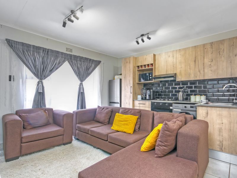 Modern open-plan living area featuring a functional kitchen with wood-finish cabinetry, black subway tile backsplash, and integrated appliances, seamlessly flowing into the lounge space.