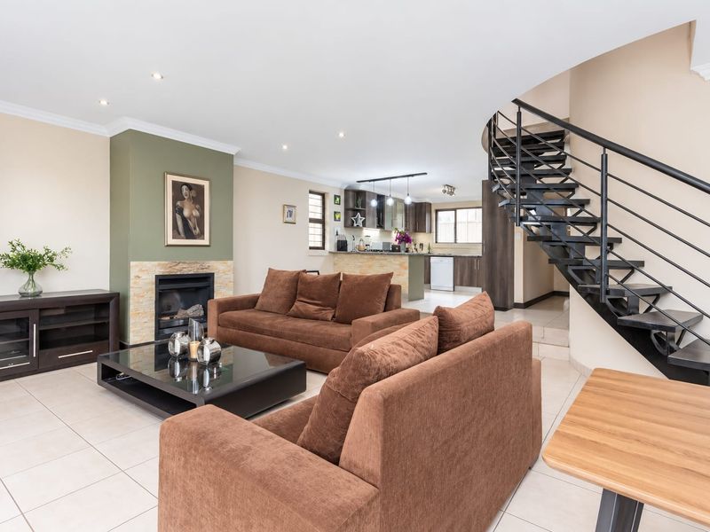 Spacious open-plan living area featuring a modern metal staircase, a stone-clad fireplace, and a functional kitchen with ample cabinetry and island seating.