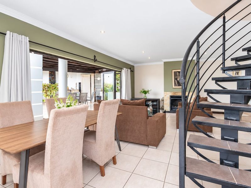 Spacious open-plan living and dining area featuring a striking spiral staircase, tiled flooring, and seamless flow to an outdoor patio through large sliding doors.