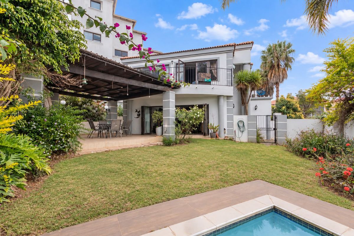 Rear view of the property featuring a covered patio, landscaped garden, swimming pool, and an upper-level balcony with wrought iron railings.