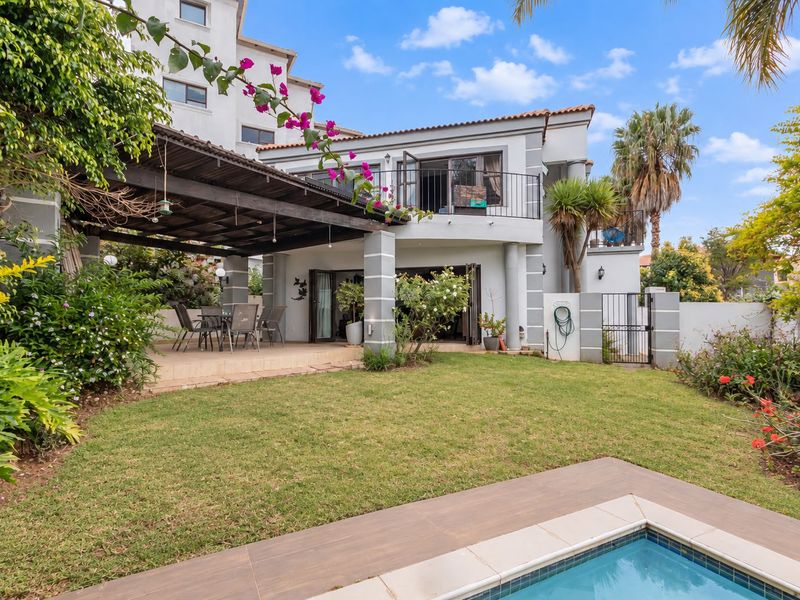 Rear view of the property featuring a covered patio, landscaped garden, swimming pool, and an upper-level balcony with wrought iron railings.
