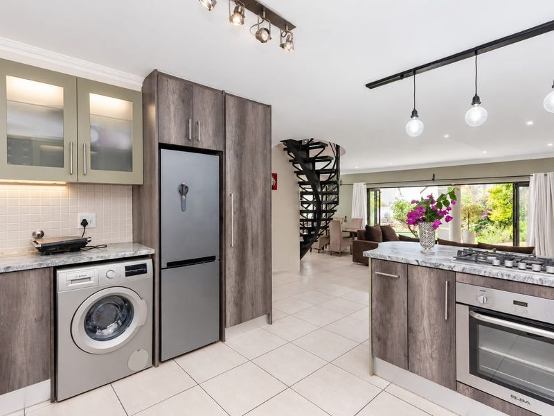 Modern open-plan kitchen featuring wood-grain cabinetry, stone countertops, integrated appliances, and a striking spiral staircase leading to the living area.