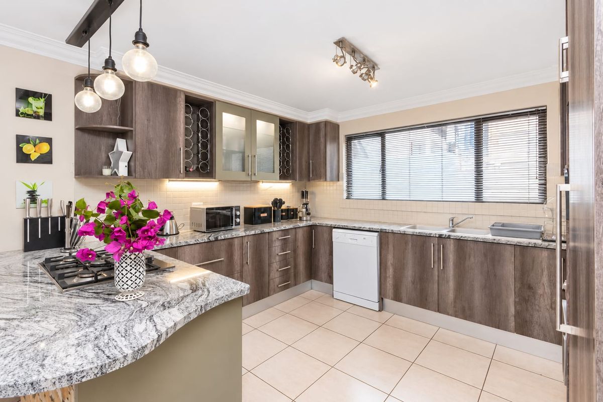 Modern kitchen featuring dark wood cabinetry, granite countertops, gas hob, and tiled flooring with ample natural light and integrated appliances.