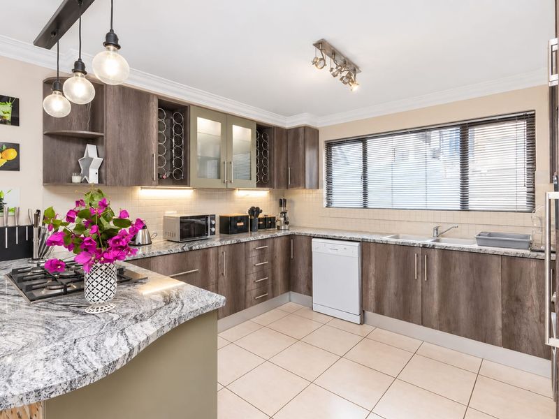 Modern kitchen featuring dark wood cabinetry, granite countertops, gas hob, and tiled flooring with ample natural light and integrated appliances.