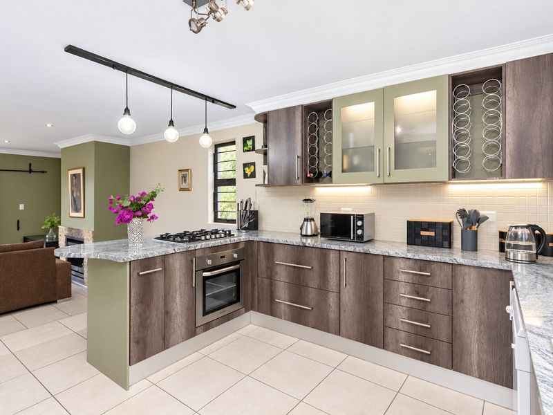 Modern open-plan kitchen featuring wood-grain cabinetry, granite countertops, integrated gas hob and oven, flowing seamlessly into a living area with a fireplace.