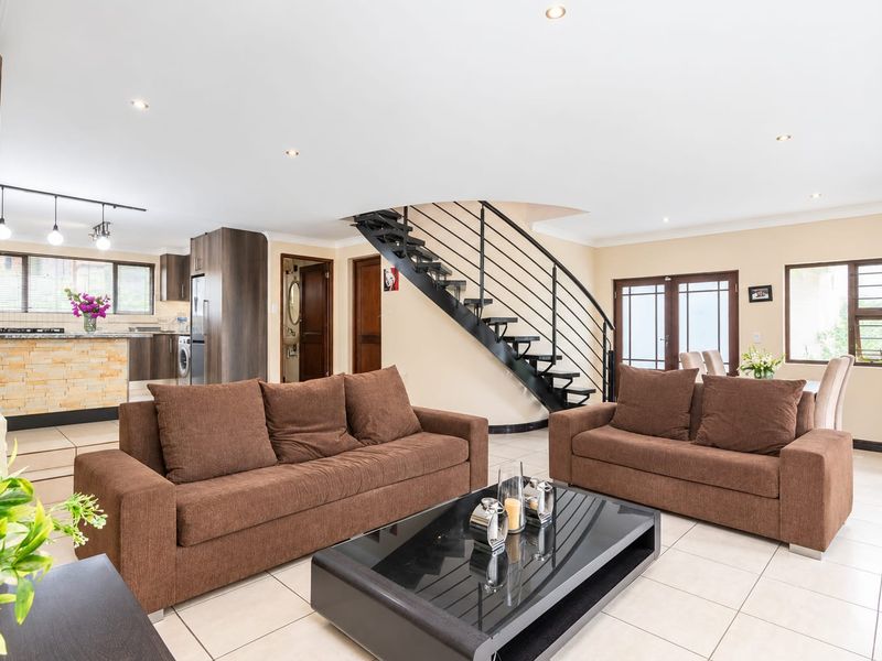Spacious open-plan living area featuring a modern staircase, tiled floors, and a well-appointed kitchen with a stone-clad island and integrated cabinetry.