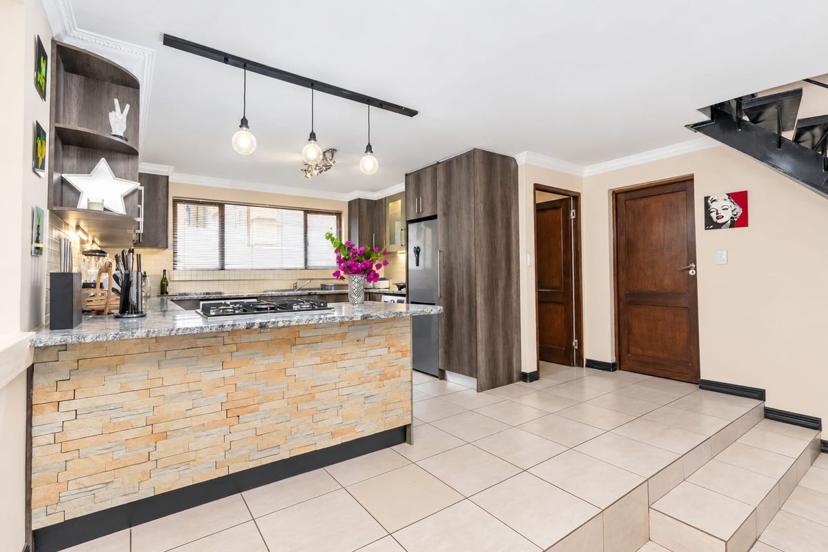 Modern kitchen featuring granite countertops, a stone-clad breakfast bar, gas hob, and ample built-in cabinetry, seamlessly integrated with the home's open-plan layout.