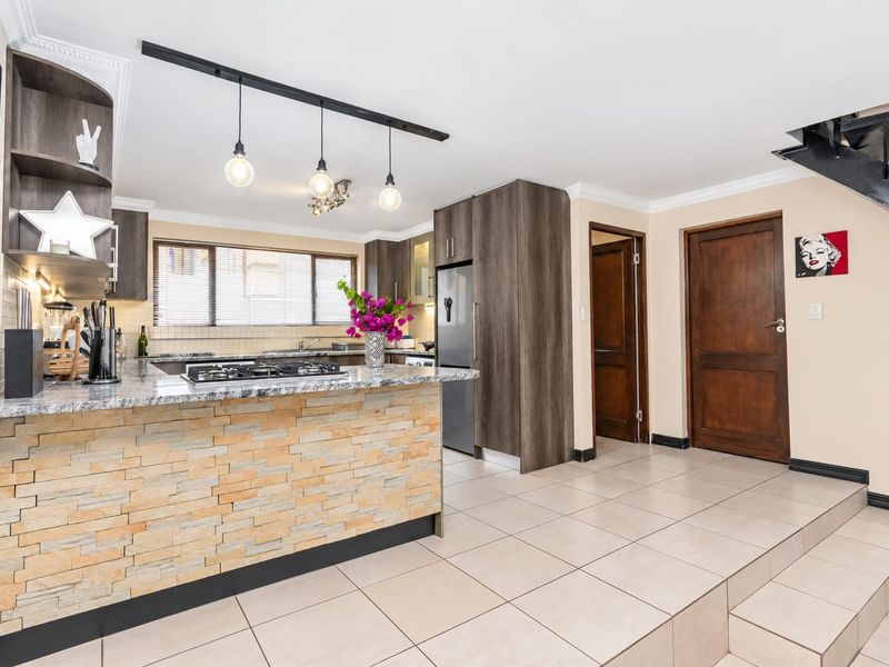Modern kitchen featuring granite countertops, a stone-clad breakfast bar, gas hob, and ample built-in cabinetry, seamlessly integrated with the home's open-plan layout.