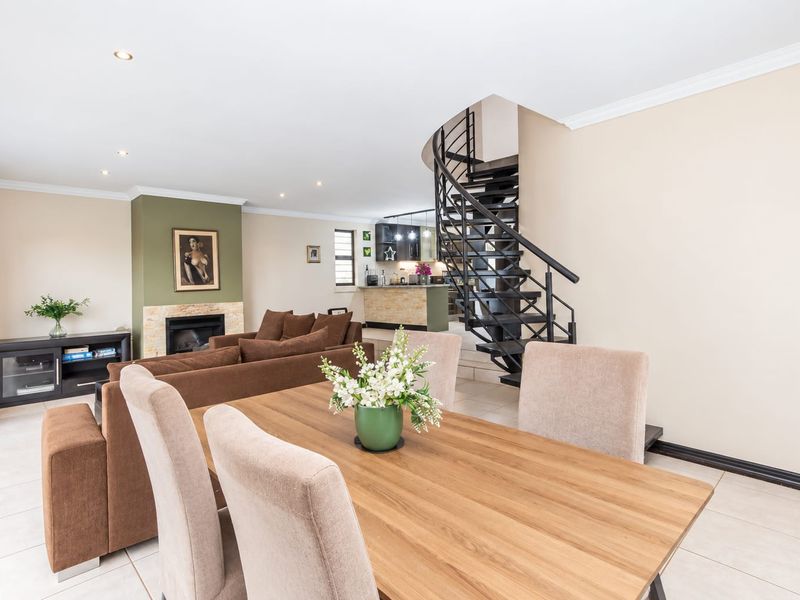 Spacious open-plan living and dining area featuring a striking black spiral staircase, a fireplace with stone detailing, and tiled flooring throughout.