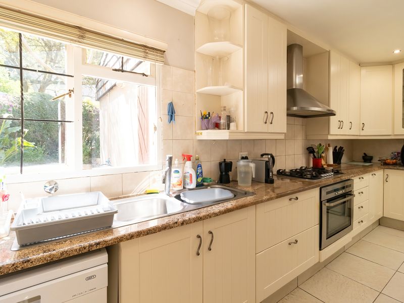 A functional kitchen featuring cream-colored cabinetry, granite countertops, a gas hob, built-in oven, and a stainless steel extractor fan with tiled flooring.