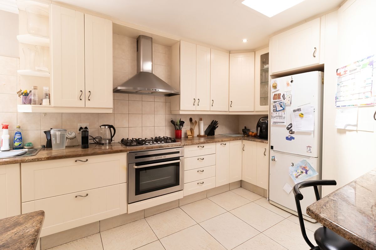 A functional kitchen featuring cream cabinetry, granite countertops, a gas hob, built-in oven, and tiled flooring with a neutral backsplash.
