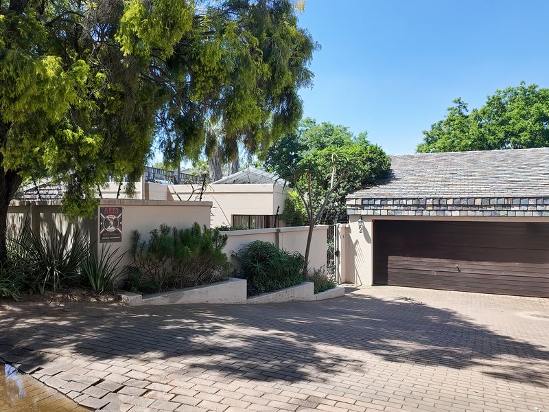 Front exterior view featuring a paved driveway, single garage with a dark door, and a perimeter boundary wall with mature landscaping.