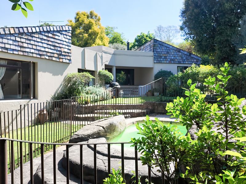 Rear exterior view featuring a rock-surrounded swimming pool, metal safety fencing, and a landscaped garden area with a tiled roof house facade.