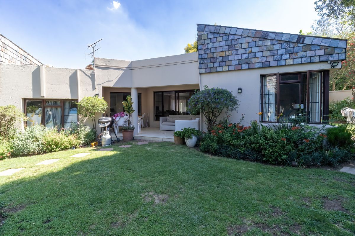 Rear view of the property featuring a covered patio, sliding glass doors, and a well-established garden with a unique tiled roof section.