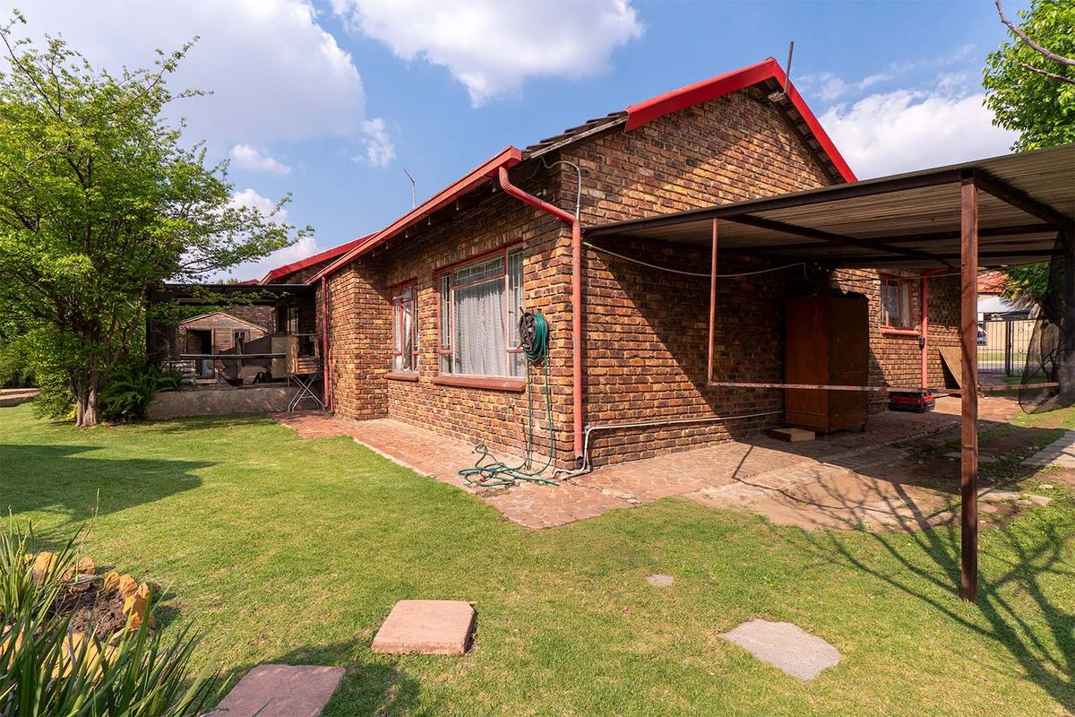 Rear view of a face brick house featuring a metal carport, paved patio area, and established garden space.