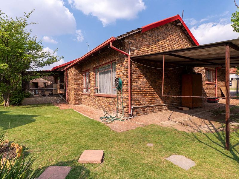 Rear view of a face brick house featuring a metal carport, paved patio area, and established garden space.